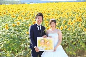 津幡町のひまわり畑の中で似顔絵を持つ新郎新婦様