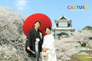 金沢城と桜を背景に版傘を持って前撮りをする新郎新婦様